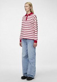 Polo de manga larga a rayas rojas y blancas con cuello, combinado con jeans de pierna ancha azul claro y zapatos negros.