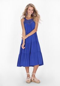 Rochie maxi albastră, fără mâneci, cu bust brodat, tiv în straturi și o croială lejeră. Purtată cu espadrile cu bretele de culoare deschisă.