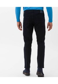 Dark blue denim jeans with a slim fit, featuring back pockets and a subtle texture. Worn with a light blue sweater and dark footwear.