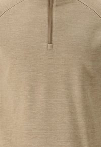 Beige pullover med højt krave og en delvis lynlås, lavet af et tekstureret stof, med en sømløs design og minimale syningsdetaljer.