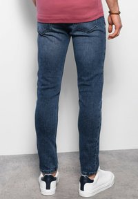 Jeans ajustados de color azul oscuro con una textura de mezclilla suave, que presentan bolsillos traseros y detalles desgastados. Combinados con zapatillas blancas.
