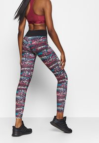 Leggings met een multicultureel abstract patroon in rood, teal en zwart, met een brede zwarte tailleband en een aansluitende pasvorm.
