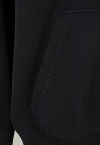 Tejido de sudadera negro con una textura suave. Cuenta con un bolsillo frontal, dobladillo acanalado y detalles de costura. Diseño sencillo, sin patrones.