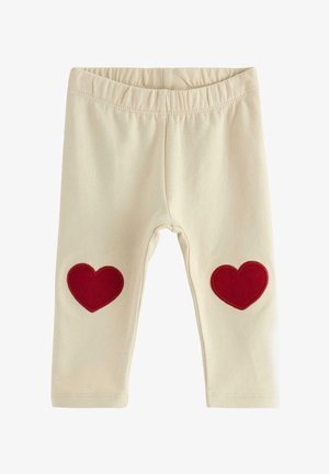 Beige leggings med en strækbar talje, der har to røde hjerteapplikationer på knæene. Blødt bomuldsstof.