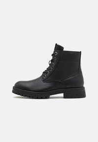 Stivaletto in pelle nera con punta tonda, occhielli in metallo e finitura texture. Suola in gomma spessa con tacche per aderenza. Logo impresso sul lato.