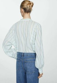 Blouse à rayures blanches et vertes avec manches bouffantes, tissu léger, col rond, associée à un jean bleu taille haute.