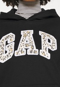 Sweat à capuche noir avec de grandes lettres "GAP" imprimées en léopard et soulignées de blanc. Tissu texturé et doublure intérieure rayée contrastante.