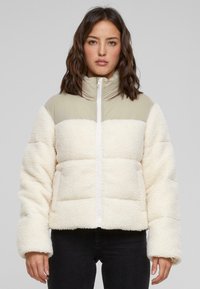 Doudoune matelassée en tissu moelleux crème avec une partie supérieure en nylon vert clair. Elle possède un col haut et une fermeture éclair à l'avant.