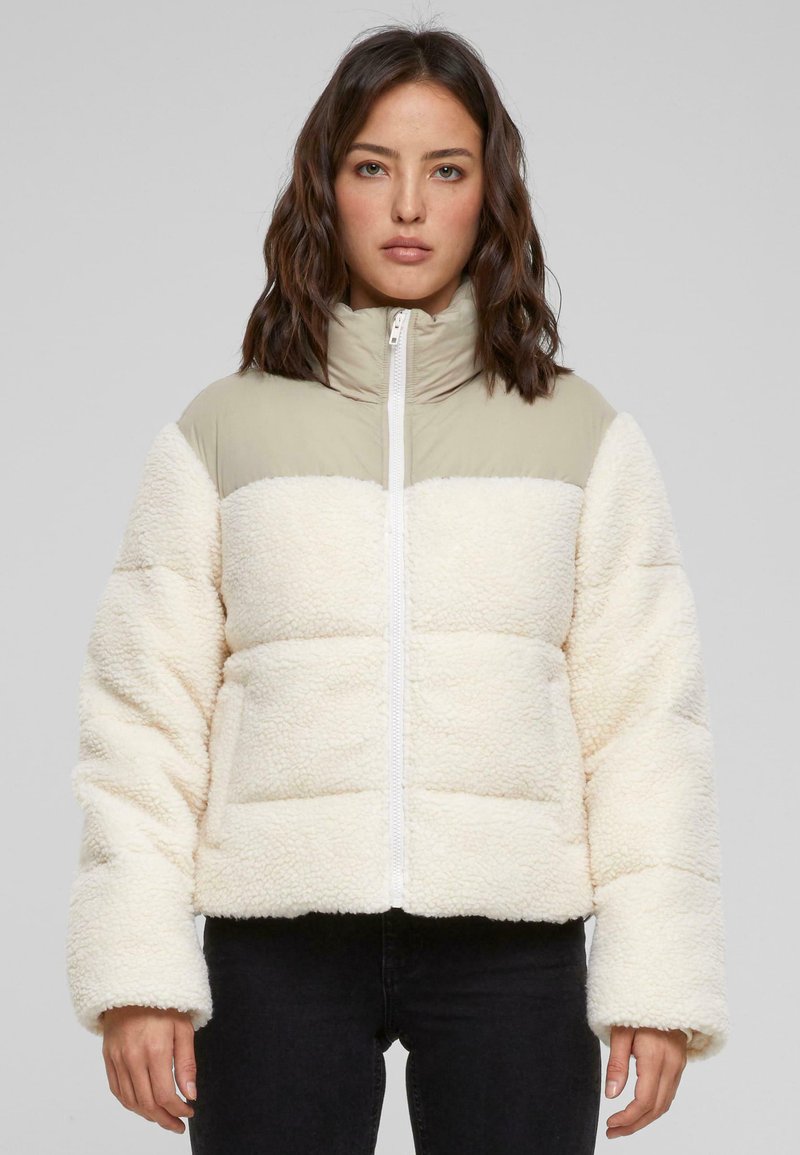Doudoune matelassée en tissu moelleux crème avec une partie supérieure en nylon vert clair. Elle possède un col haut et une fermeture éclair à l'avant.