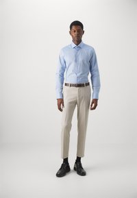 Lys blå langermet skjorte, beige skreddersydde bukser, svart belte og svarte sko med snøring. Enkelt stoff, tettsittende design og rett snitt.