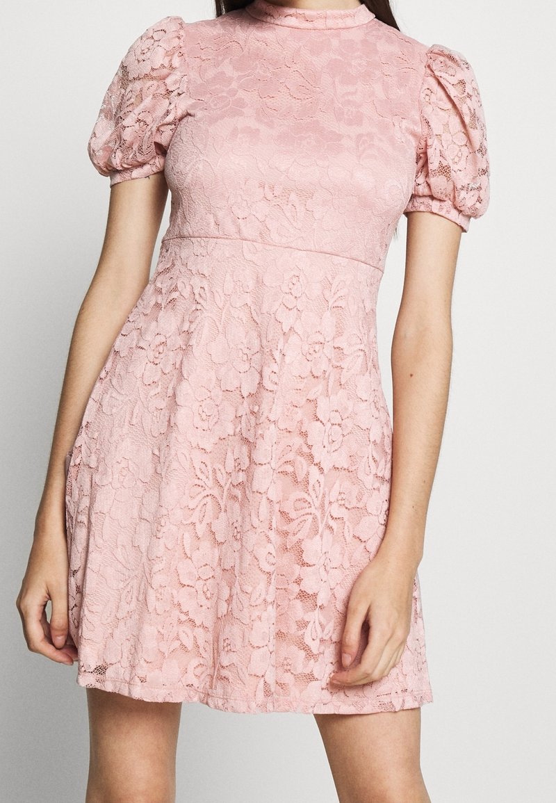Spitzenkleid in zartem Rosa, mit tailliertem Oberteil und ausgestelltem Rock. Puffärmel und florales Muster verleihen Textur und Detail.