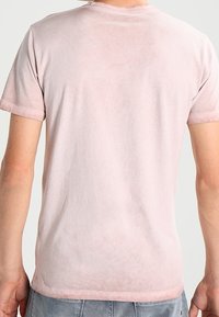 Kortärmad t-shirt i mjuk rosa färg av bomull, med rund halsringning och en något urtvättad textur på baksidan, utan synliga logotyper eller mönster.