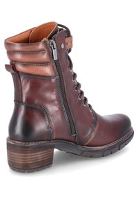 Botas de cuero marrón hasta el tobillo con cremallera lateral, parte frontal con cordones, tacón marrón y ligeros detalles de costura en el eje y la punta. Acentos texturizados.