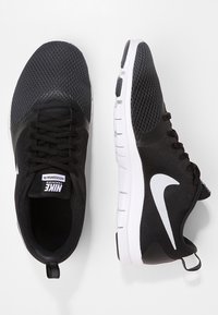 Czarne sportowe buty z siateczki z białym logo Nike, wyposażone w teksturowaną cholewkę, zawiązywane na sznurowadła oraz z białą, amortyzowaną podeszwą zewnętrzną.