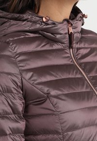 Pikowana, lekka kurtka w stonowanym kolorze mauve z zamkiem błyskawicznym z przodu i kapturem. Posiada różowo-złote akcenty oraz elastyczne wykończenie kaptura.