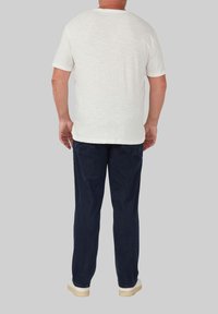 Witte t-shirt met korte mouwen en een ronde halslijn, gecombineerd met donkerblauwe broek, gezien vanuit de rug. Geweven stofdetails zichtbaar.