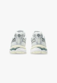 Scarpe sportive bianche con materiale in mesh testurizzato, dettagli argentati e suola in gel trasparente. Progettate per il comfort con un tallone arrotondato e supporto imbottito.