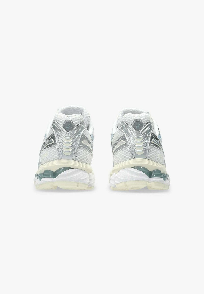 Scarpe sportive bianche con materiale in mesh testurizzato, dettagli argentati e suola in gel trasparente. Progettate per il comfort con un tallone arrotondato e supporto imbottito.