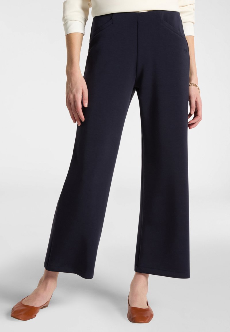 Široké navy kalhoty vyrobené z měkké látky, mají přední kapsy a hladký pas. Dokončeny s čistým lemem, kombinované s hnědými balerínami.