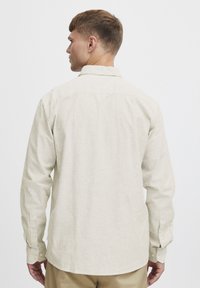 Lys beige langærmet skjorte med smalle lodrette striber, knappede manchetter og klassisk krave. Glat stofstruktur.