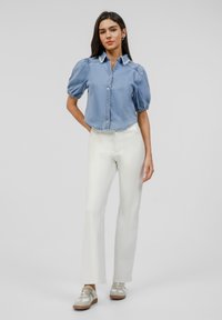 Light blue denim shirt with puff sleeves, button-up design, and frayed collar. Paired with white straight-leg pants and beige sneakers.