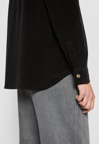 Zwarte corduroy shirt met een knoopmanchet, voorzien van een licht gebogen zoom en een textuur, gecombineerd met grijze broek.