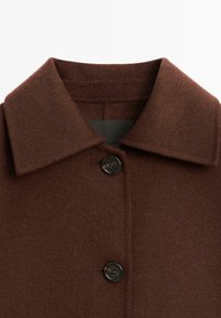 Bruine wollen jas met een klassieke kraag, twee knopen en een zachte textuur, ontworpen voor warmte en comfort.