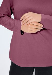 Langärmeliges, rundhalsausschnittiges Oberteil in einem tiefen Mauve-Ton. Baumwollmischgewebe mit glatter Textur. Verfügt über eine lockere Passform und einen seitlichen Schlitz am Saum.