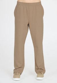 Lichte, bruine, elastische broek met zijzakken, rechte pijpen en een zachte textuur. Gecombineerd met beige sneakers.