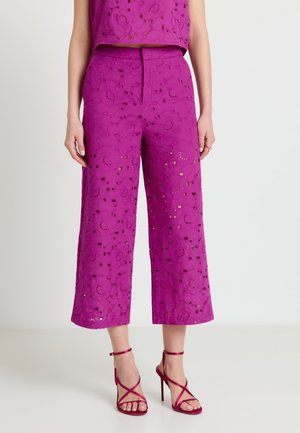 Pantaloni corti a gamba larga di un rosa acceso con ricamo floreale traforato, indossati con sandali con tacco alto e cinturini abbinati.