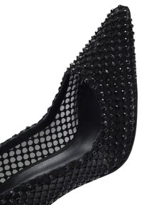 Chaussure noire à talons hauts avec un bout pointu, des détails en maille et ornée de sequins noirs sur la surface supérieure. Doublure intérieure lisse.