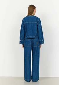 Jeans jakna in široki hlače iz temno modrega denima. Značilnosti vključujejo skrajšano jakno z navpičnimi žepi in krožnim logotipom na zadnjem žepu.