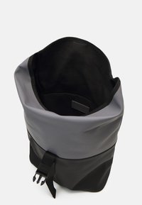 Svart og grå rull-topptaske laget av vanntett materiale, med en sikker spenne-lukking, glatt tekstur, og et mykt, uforet indre.