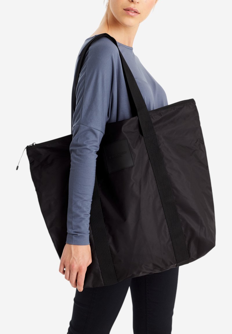 Duża czarna torba tote wykonana z nylonu, wyposażona w zamek błyskawiczny, solidne paski na ramię i minimalistyczny design z metką marki.