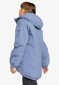 Veste en duvet bleue claire avec capuche, poignets élastiques et logo Roxy sur la manche. Présente un design boxy et une texture douce et lisse.