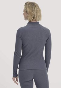 Graues Langarmoberteil aus geripptem Material mit hohem Kragen und figurbetontem Design, kombiniert mit passenden Unterteilen.
