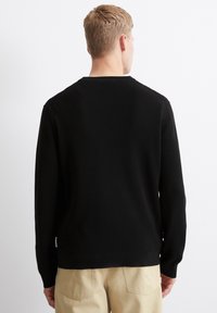 Schwarzer, strukturierter Pullover mit langen Ärmeln und Rundhalsausschnitt, ausgestattet mit einem gerippten Saum und Bündchen. Sichtbares Etikett an der Seite. Lässiges Design.