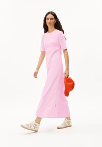 Pink maxi dress with short sleeves, straight cut, side slit; worn with an orange cap and white perforated shoes. Smooth fabric texture.