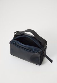 Navyblaue, glänzende Kulturbeutel aus weichem Synthetikmaterial mit Reißverschluss und einem schwarzen Gummigriff. Verfügt über ein minimalistisches Design.