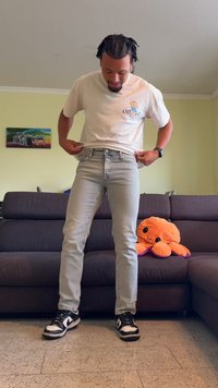 Jeans de culoare bleu deschis, cu o croială ajustată, purtate cu un tricou alb. Tenisi alb-negru. Un caracatiță pufoasă portocalie pe un canapea închisă la culoare în fundal.