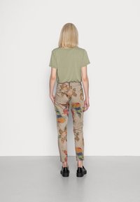 Groene katoenen t-shirt gecombineerd met beige cargo broek met een kleurrijke bloemen- en luipaardprint. Zwarte schoenen maken de look compleet.