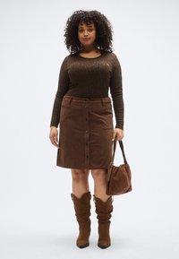 Fustă maro din catifea cu nasturi în față, combinată cu un top cu mâneci lungi și imprimeu de leopard închis la culoare. Cizme maro casual și o geantă de umăr asortată.