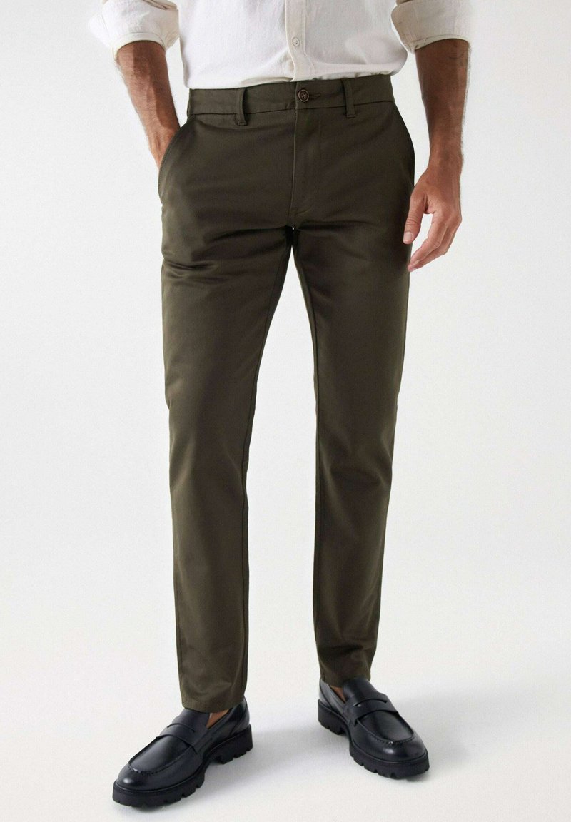 Olijfgroene, slim-fit broek gemaakt van gladde stof, met een standaard tailleband en zijzakken. Gecombineerd met zwarte instappers.