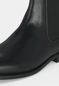 Bottine Chelsea noire en cuir avec panneau latéral élastique et petit talon bloc, vue en gros plan sur fond blanc.
