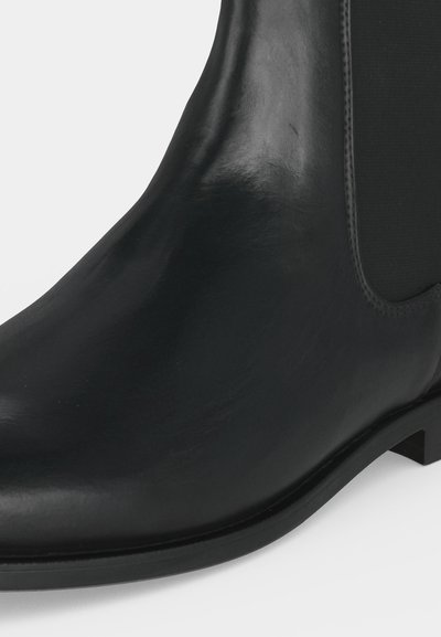 Bottine Chelsea noire en cuir avec panneau latéral élastique et petit talon bloc, vue en gros plan sur fond blanc.