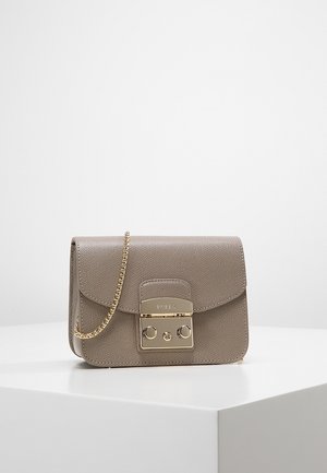Petit sac à main en cuir taupe avec bandoulière chaîne dorée et fermoir rectangulaire doré sur surface blanche et fond uni.