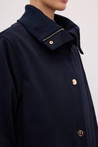 Marinefrakke med høj krave, udstyret med en gylden lynlås og knapper. Materialet ser glat ud med en struktureret design, der fokuserer på enkelhed.