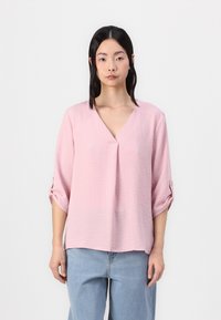 Lys rosa, teksturert bluse med V-hals og trekvartlange ermer. Ermene er rullet opp og har knappdetaljer. Ledig passform.