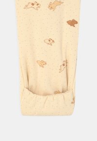 Ljusgula leggings med mjuk textur, prydda med spridda bruna kaniner och små blåa prickar. Elastisk mudd i nederkanten.