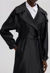 Čierny saténový trench coat s širokým golierom, dvojradovými gombíkmi, opaskom v páse a manžetami s ohrnutím. Obsahuje bočné vrecká.